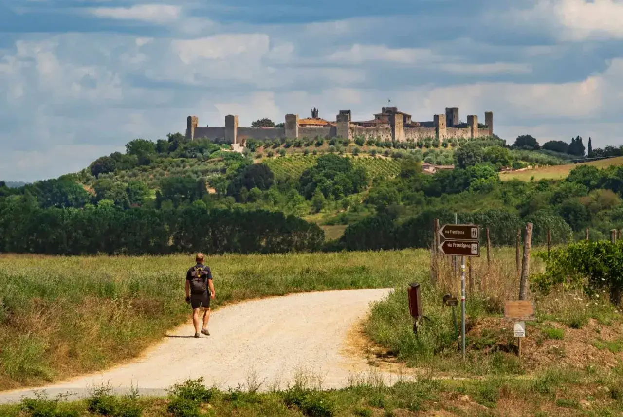 Un randonneur marche sur un chemin de terre vers le village fortifié de Monteriggioni, en Italie.