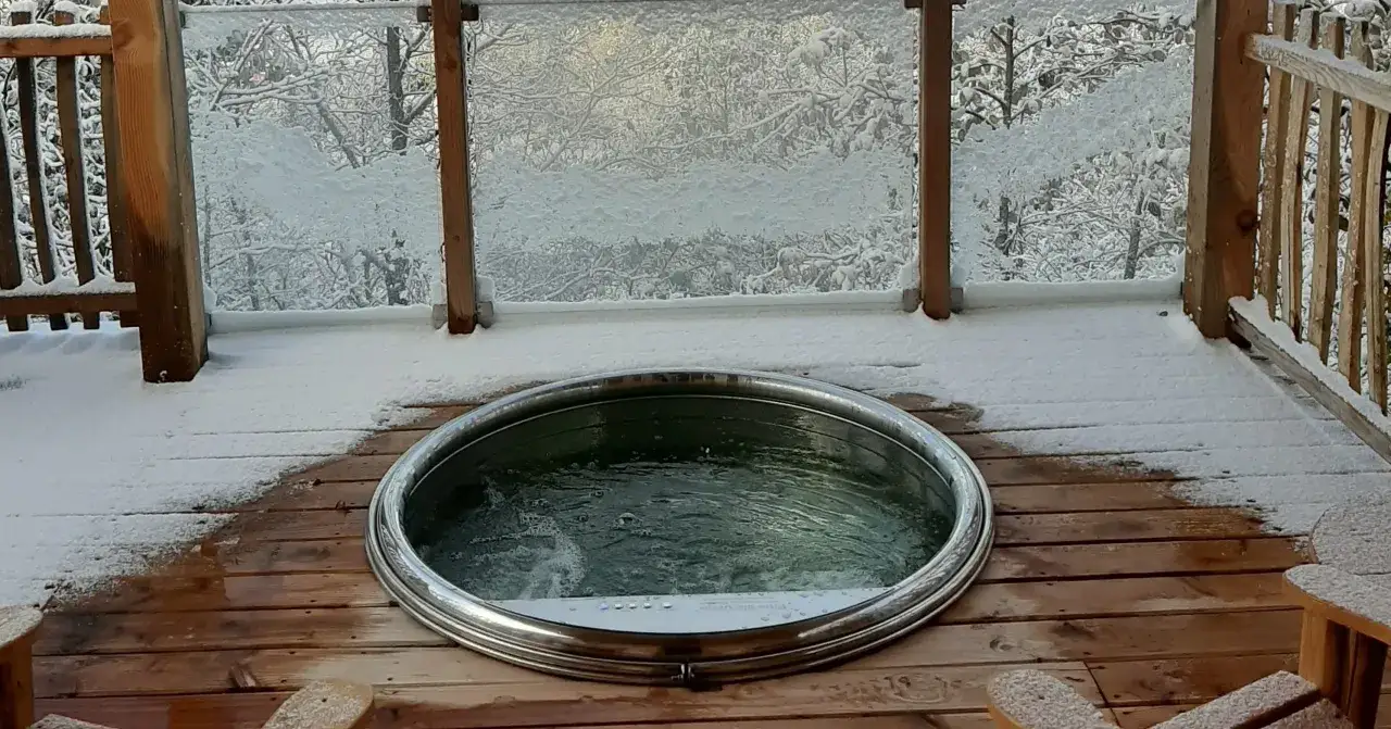 Jacuzzi fumant sur une terrasse enneigée, un lieu insolite dans le Jura, offrant un contraste saisissant entre le froid extérieur et la chaleur de l'eau.
