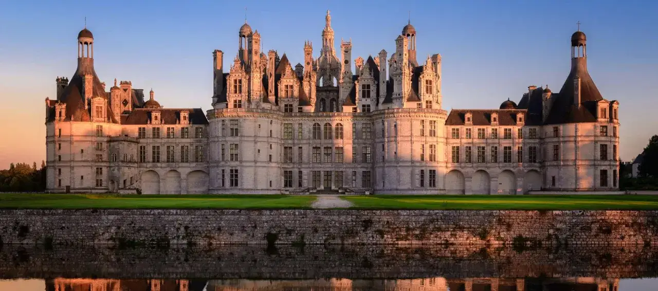 Le château de Chambord, un des plus célèbres châteaux en France, se reflète dans l'eau au coucher du soleil.