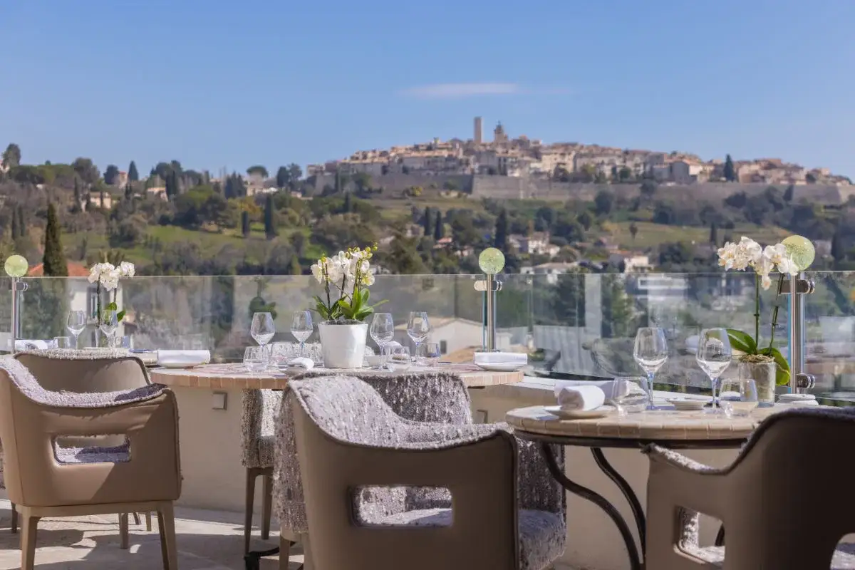 Tables dressées pour un repas en terrasse, avec vue sur le village perché de Saint-Paul-de-Vence. L'élégance des restaurants de Saint-Paul-de-Vence.