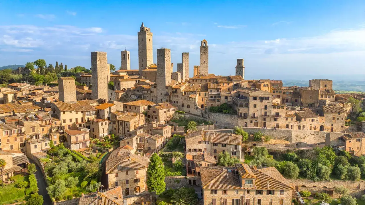 Vue a&eacute;rienne de Civitella in Val di Chiana, un village m&eacute;di&eacute;val toscan avec ses tours embl&eacute;matiques et ses toits de tuiles ocres sous un ciel bleu.