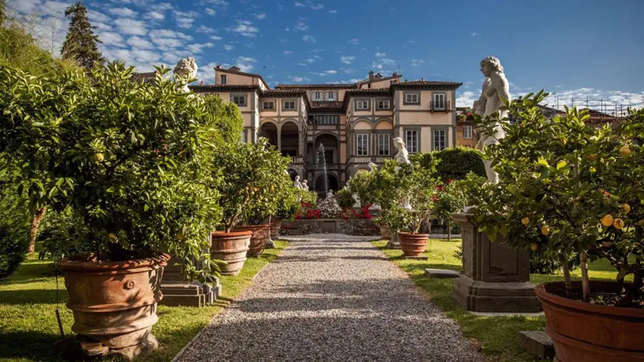 Jardin luxuriant menant au Palazzo Pfanner, avec des arbres en pot, des statues et une fontaine.