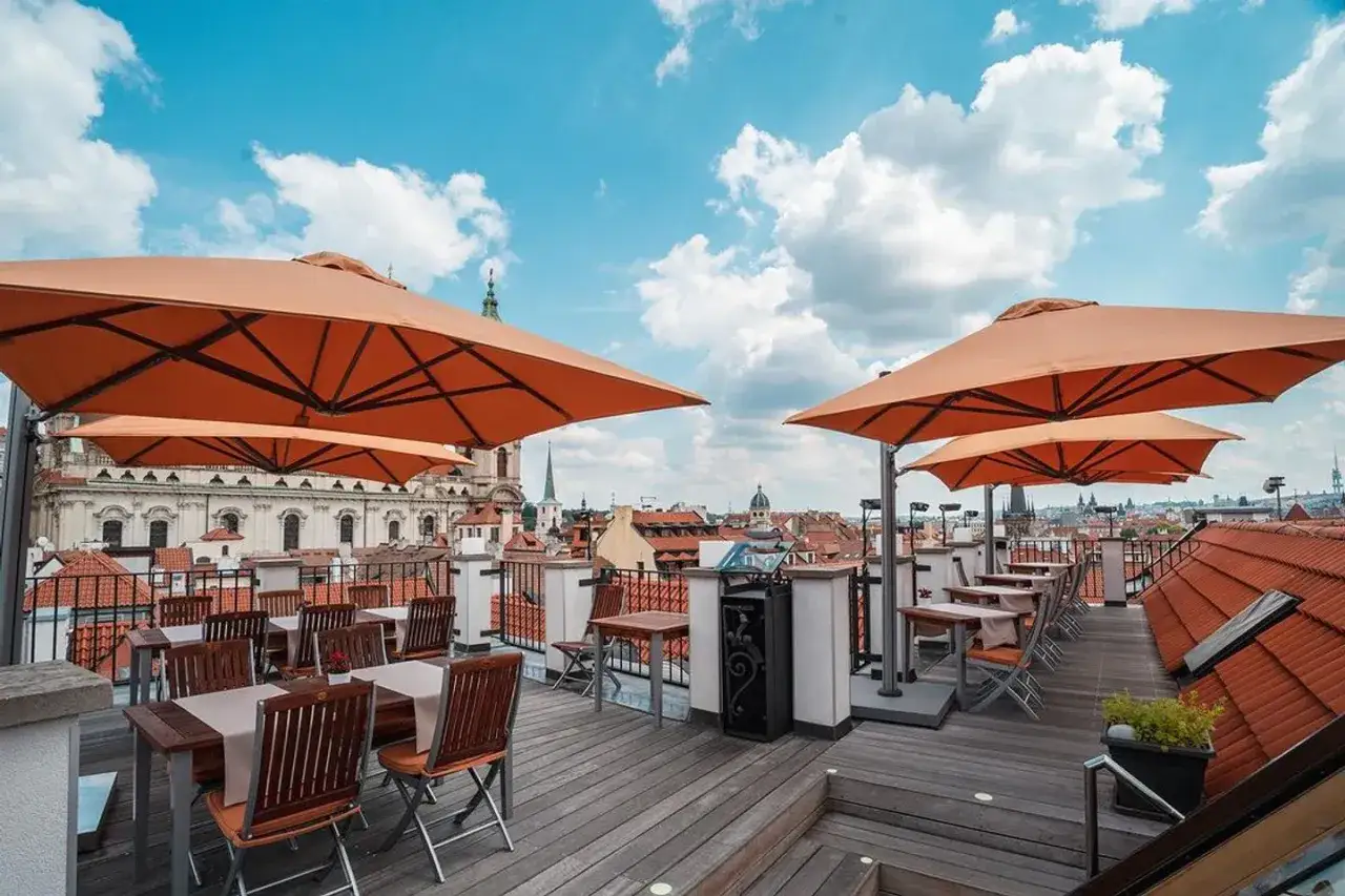 Terrasse d'un bon restaurant à Prague, avec des tables dressées sous de grands parasols orange, offrant une vue imprenable sur les toits et les églises de la ville.