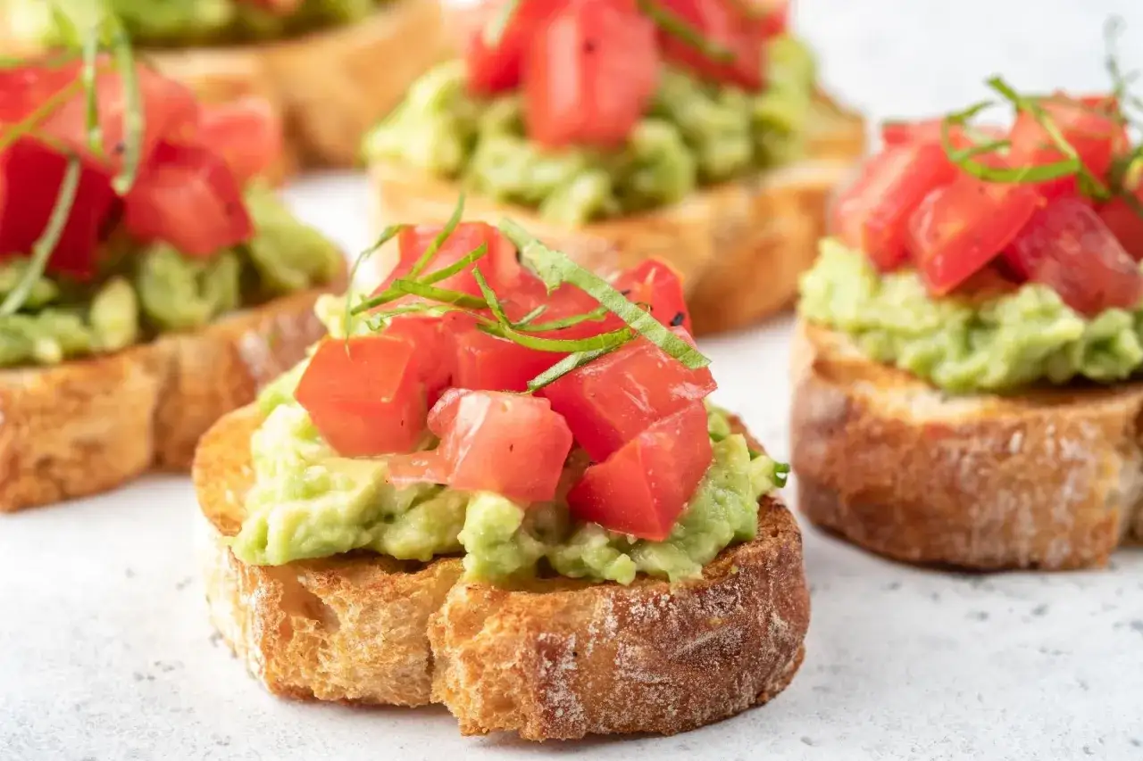 Crostini toscani : toasts grillés garnis d'avocat écrasé et de dés de tomates fraîches, parsemés de basilic ciselé.