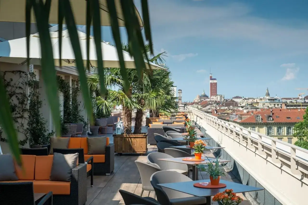 Terrasse ensoleillée avec vue sur Turin, idéale pour savoir où manger à Turin. Palmiers et mobilier confortable invitent à la détente.