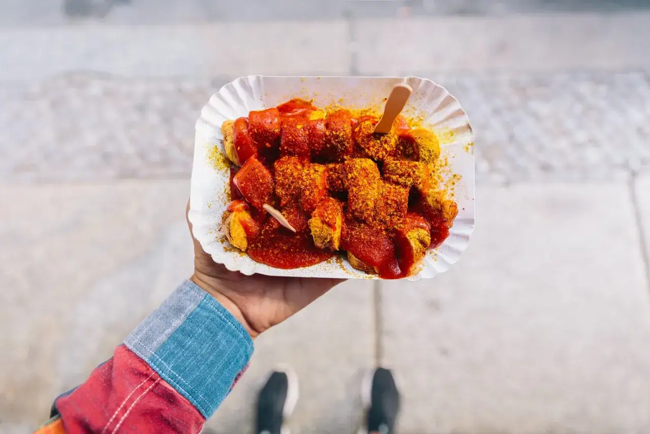 Currywurst, un classique pour savoir où manger à Berlin. Servi dans un plateau en carton, avec une sauce tomate épicée et du curry en poudre.