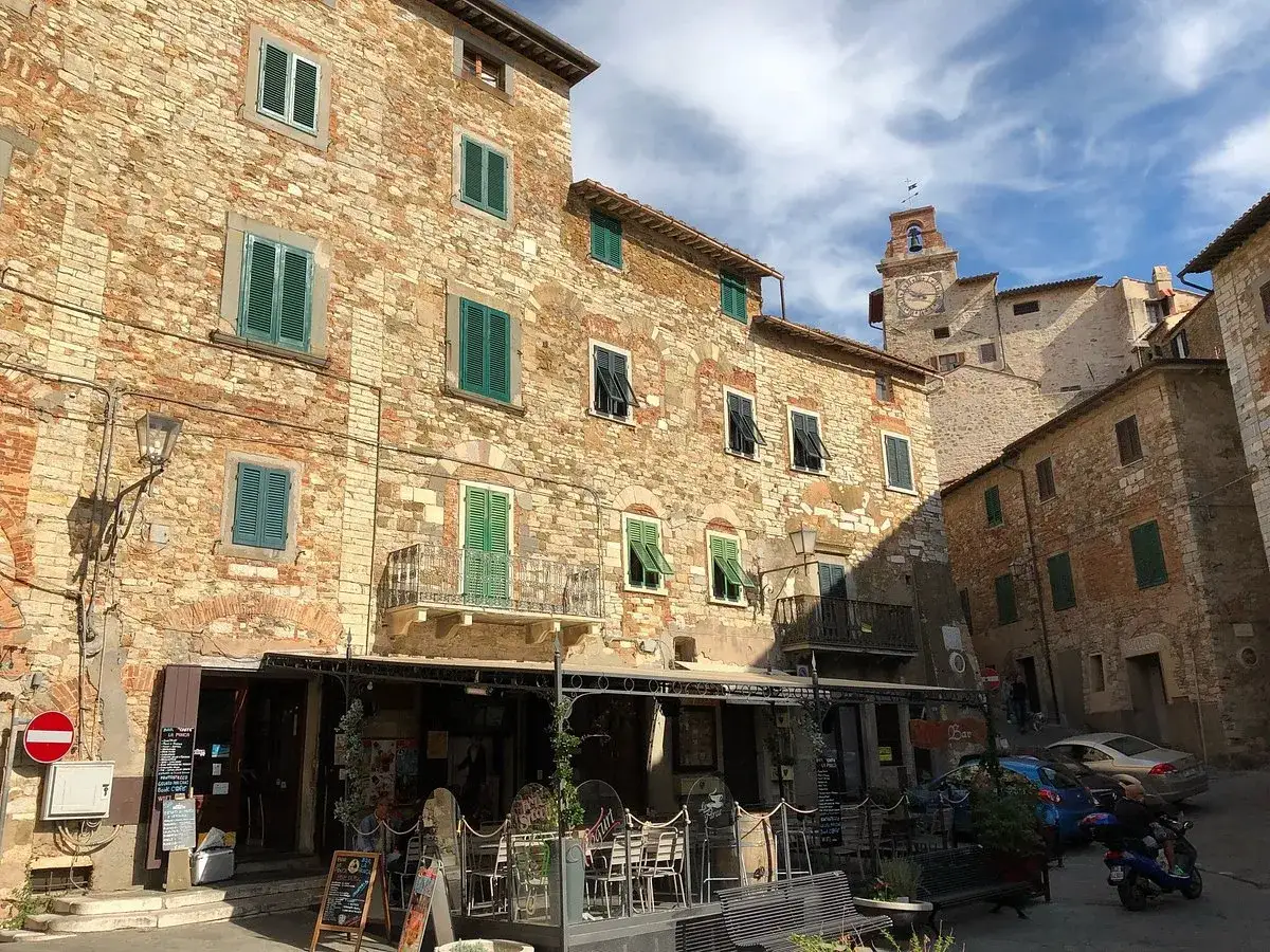Ruelles ensoleillées de Campiglia Marittima, avec des bâtiments en pierre, des volets verts et une tour d'horloge médiévale.