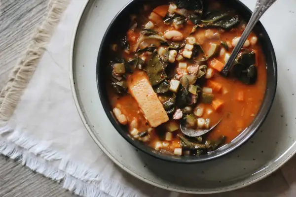 Un bol de ribollita toscana, une soupe épaisse et réconfortante avec des légumes verts, des haricots et des pâtes, servie avec une cuillère.