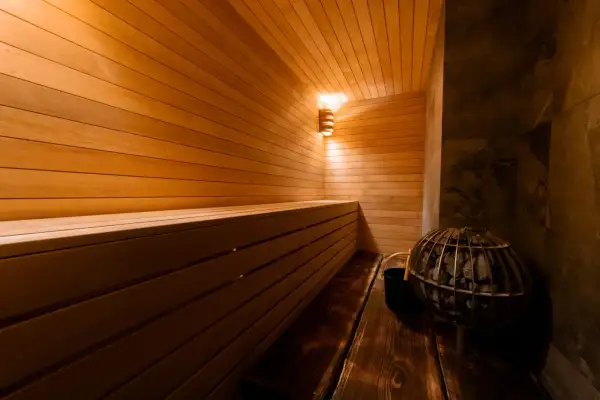 Intérieur d'une **sauna Prague** chaleureuse, avec des bancs en bois clair, un poêle à pierres et un éclairage doux.