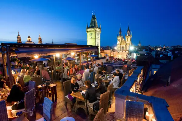 Dîner sur un rooftop à Prague, avec vue sur la tour de l'horloge et l'église Notre-Dame du Týn. Ambiance chaleureuse.