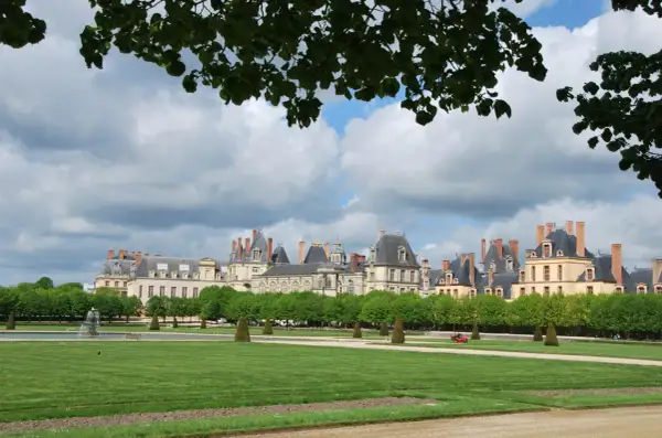 Magnifique vue du château de Fontainebleau, idéal pour visiter. Pelouse verdoyante, fontaine et arbres taillés.