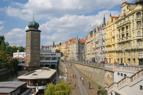 Vue animée de la Vltava, idéale pour visiter Prague en 1 jour. La tour de la Poudrière et les façades colorées des immeubles bordent la promenade.