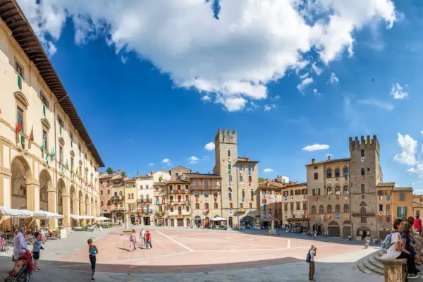 La Piazza Grande d'Arezzo, avec ses tours médiévales et ses arcades, sous un ciel bleu. Ici, la vie est belle, rythmée par les pas des passants.