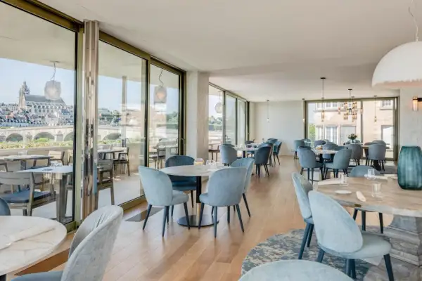 Salle lumineuse avec vue panoramique sur la Loire. Tables dressées, chaises bleues confortables. Un cadre idéal pour découvrir les restaurants de la Loire.