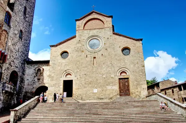 Le majestueux **duomo San Gimignano** se dresse sous un ciel bleu éclatant, ses marches invitant à la découverte de son histoire.