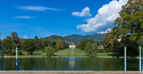 Le parc de la villa reale di Marlia s'étend devant un étang paisible, avec une fontaine jaillissant au centre. Des arbres majestueux bordent la pelouse menant à la villa.