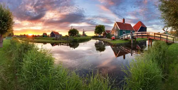 Coucher de soleil sur un canal bordé de roseaux, avec des moulins et des maisons traditionnelles, un aperçu des plus belles villes des Pays-Bas.