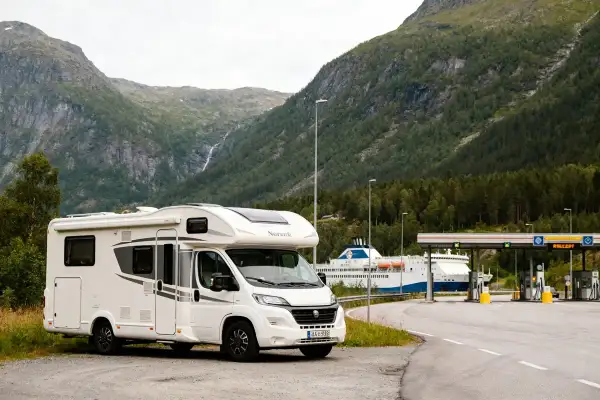 Camping-car blanc prêt pour un road trip en Norvège en camping-car budget, avec un ferry et des montagnes en arrière-plan.