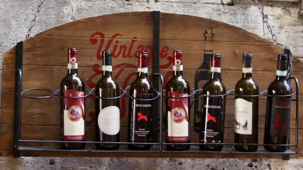 Huit bouteilles de vin, dont plusieurs de **vin de Toscane**, alignées sur une étagère en bois ornée d'une inscription "Vintage".