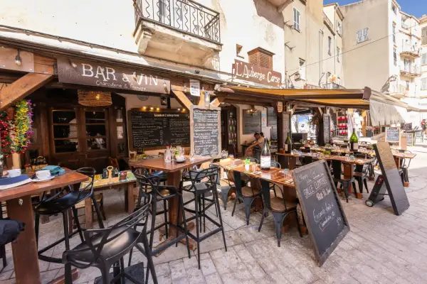 Terrasse d'un restaurant "Bar à Vin" dans le restaurant bonifacio vieille ville. Tables dressées, chaises noires, ardoises de menu. Ambiance estivale.