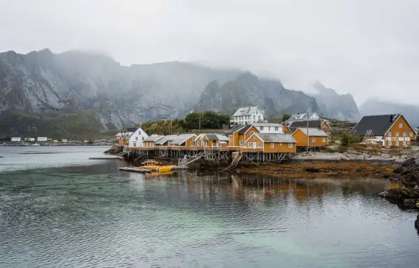 Maisonnettes jaunes sur pilotis, reflets dans l'eau, montagnes brumeuses en arrière-plan. Idéal pour un budget voyage îles Lofoten.