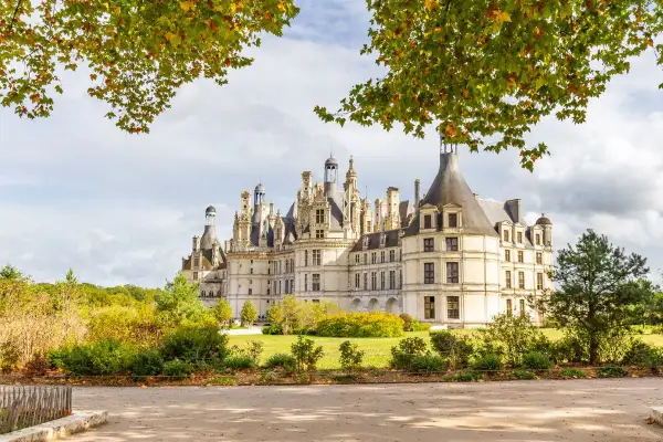 Magnifique château avec ses nombreuses tours et tourelles, entouré d'arbres aux couleurs d'automne. Un paysage de rêve.