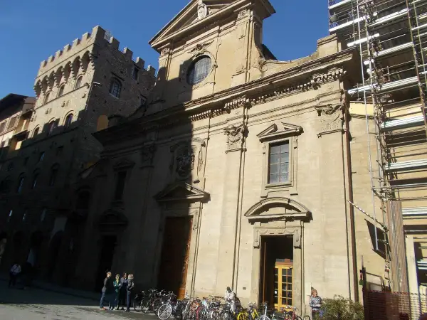 Façade de la basilique Santa Trinita à Florence, avec des échafaudages sur le côté droit. Des vélos sont garés devant.