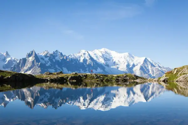 Un randonneur en rouge célèbre la beauté de cet endroit paradisiaque en France, avec le Mont Blanc majestueux se reflétant dans un lac alpin paisible.