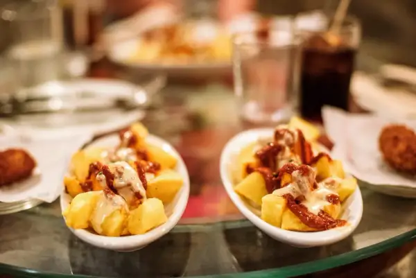 Patatas bravas, un classique pour savoir où manger à Barcelone. Des tapas savoureuses sur une table en verre.