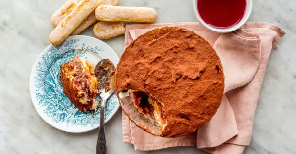 Délicieuse zuppa inglese recette, avec une part déjà servie sur une assiette ornée. Des biscuits à la cuillère et une coupelle de coulis complètent ce dessert gourmand.