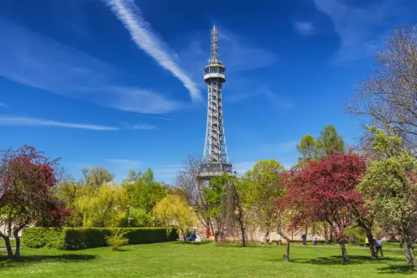 La tour Eiffel de Prague, une structure métallique imposante, se dresse fièrement au milieu d'un parc verdoyant et fleuri sous un ciel bleu éclatant.