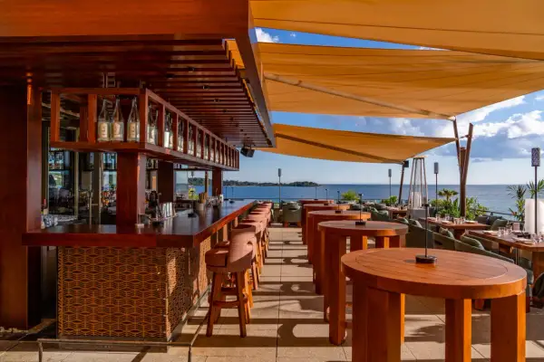Bar de plage à Cannes avec vue sur la mer. Tables en bois, tabourets de bar et voiles d'ombrage.