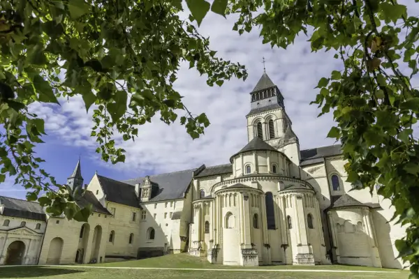 Le majestueux **château de Fontevraud**, avec sa tour imposante et ses arcs romans, se dresse sous un ciel bleu parsemé de nuages, encadré par le feuillage verdoyant des arbres.