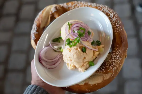 Un plat de fromage à tartiner avec des oignons rouges et de la ciboule, servi avec un bretzel salé, parfait pour un beer garden.