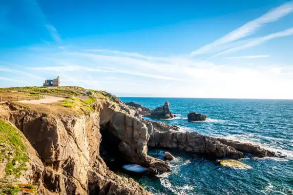 Falaises rocheuses et ruines d'un bâtiment sur une colline surplombant la mer bleue. Idéal pour savoir que faire à Quiberon ce week-end.