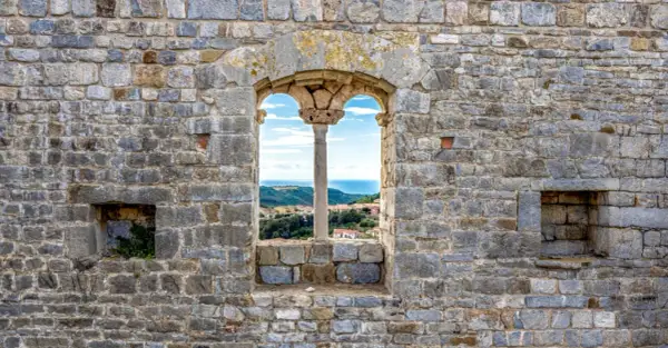 Fenêtre médiévale à Campiglia Marittima offrant une vue sur la mer et les toits du village.