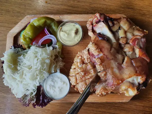 Un plat tcheque copieux : un jarret de porc rôti à la peau croustillante, servi avec de la choucroute, des poivrons, des oignons rouges et deux sauces.