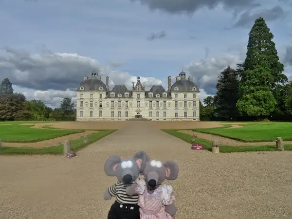 Deux souris en peluche devant le majestueux château de Cheverny, un jour de ciel nuageux.