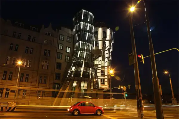 La **maison dansante Prague** s'illumine la nuit, une voiture rouge passe devant, créant une scène urbaine animée.