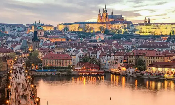 Prague en ce moment : le pont Charles animé, le château illuminé et la Vltava reflétant les lumières de la ville.