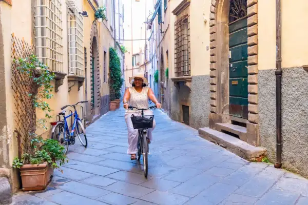 Une femme souriante fait du vélo dans une ruelle pavée, profitant d'une belle journée à Florence.