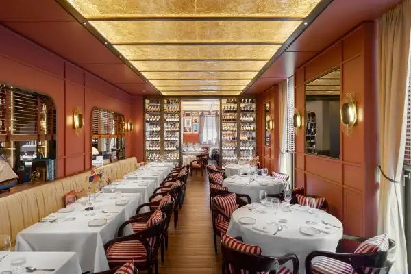 Intérieur d'un restaurant typique Milan, tables dressées, murs corail, étagères à vin illuminées et plafond dorée.