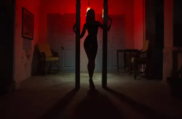 Silhouette d'une femme dans un décor rouge, évoquant l'ambiance du quartier rouge de Prague. Des chaises et des portes bleues créent un contraste saisissant.