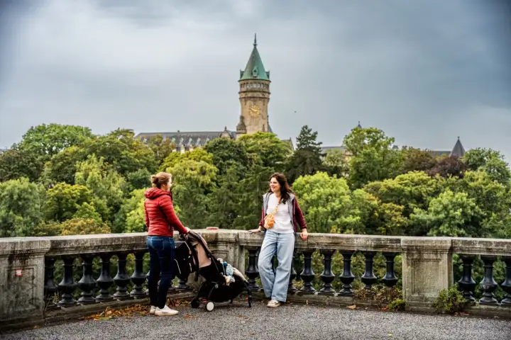 Deux femmes discutent près d'une poussette, avec une vue sur le Palais de la Banque d'État. Un aperçu de ce que l'on peut voir en visiter le Luxembourg en 3 jours.
